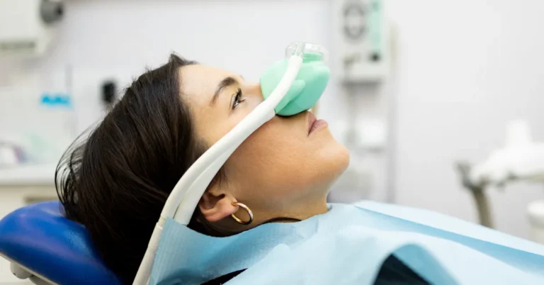 Female patient receiving nitrous oxide (laughing gas) sedation through a nasal mask while reclining in a dental chair.