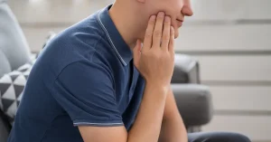Young man touching his cheek due to jaw pain caused by impacted wisdom teeth.